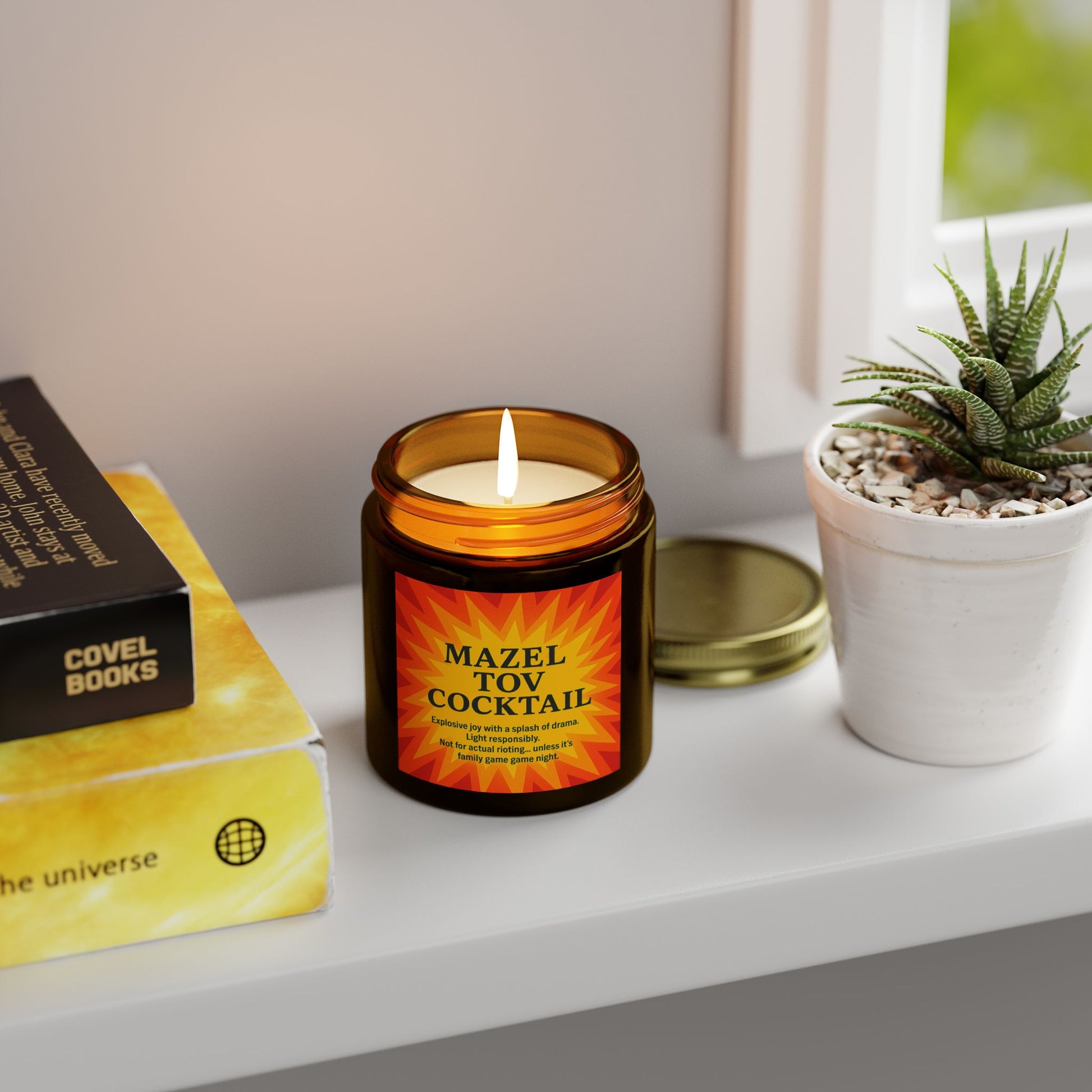 Candle labeled 'Mazel Tov Cocktail' on a shelf with books and a plant