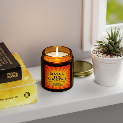 Candle labeled 'Mazel Tov Cocktail' on a shelf with books and a plant