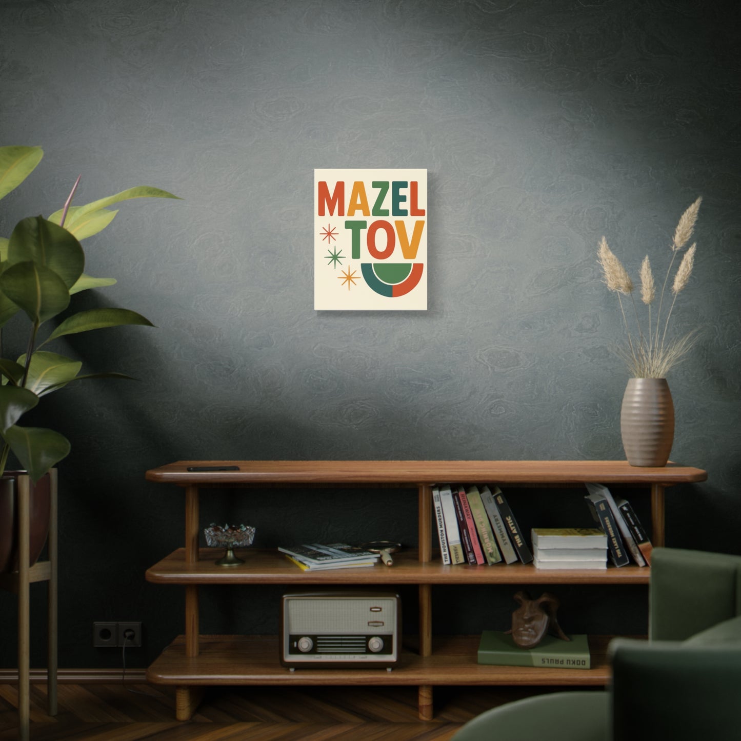 Decorative poster with 'Mazel Tov' text on a wall above a wooden shelf with books and a plant.