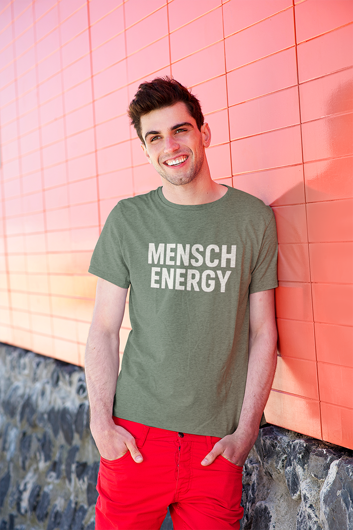Man wearing a green t-shirt with 'MENSCH ENERGY' text against a pink tiled wall.