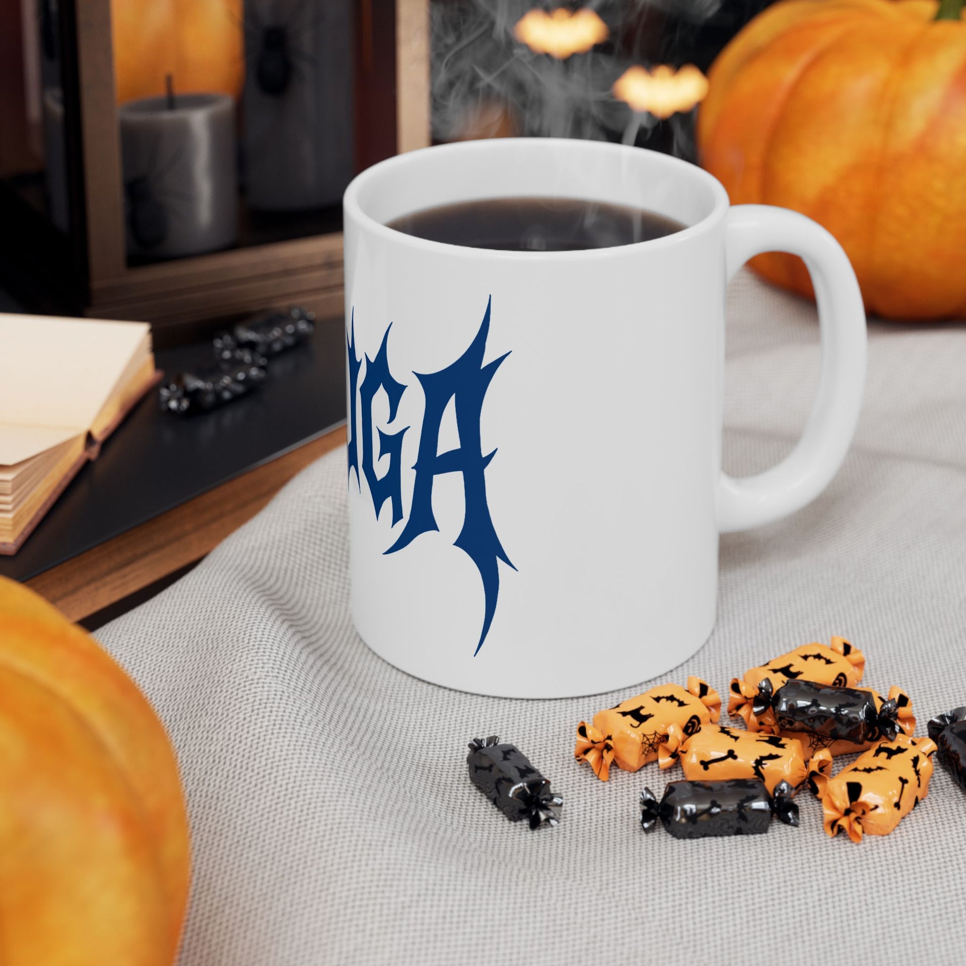 White mug with blue 'meshuga' logo on a table with Halloween-themed treats and pumpkins.