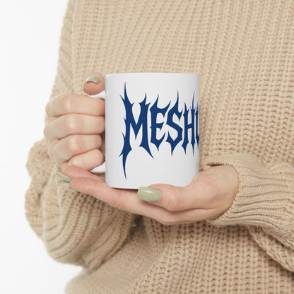 Person holding a white mug with blue text 'meshuga' against a beige background