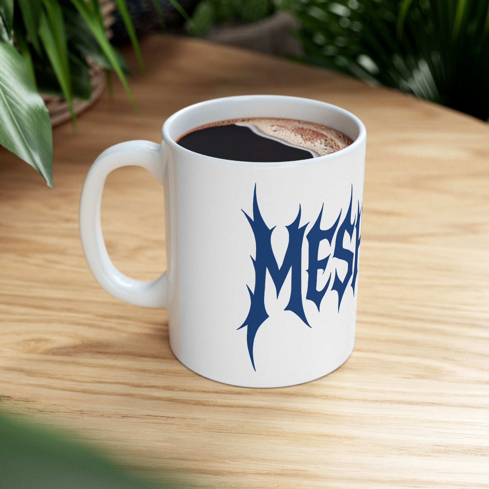 White mug with 'meshuga' in blue text on a wooden table