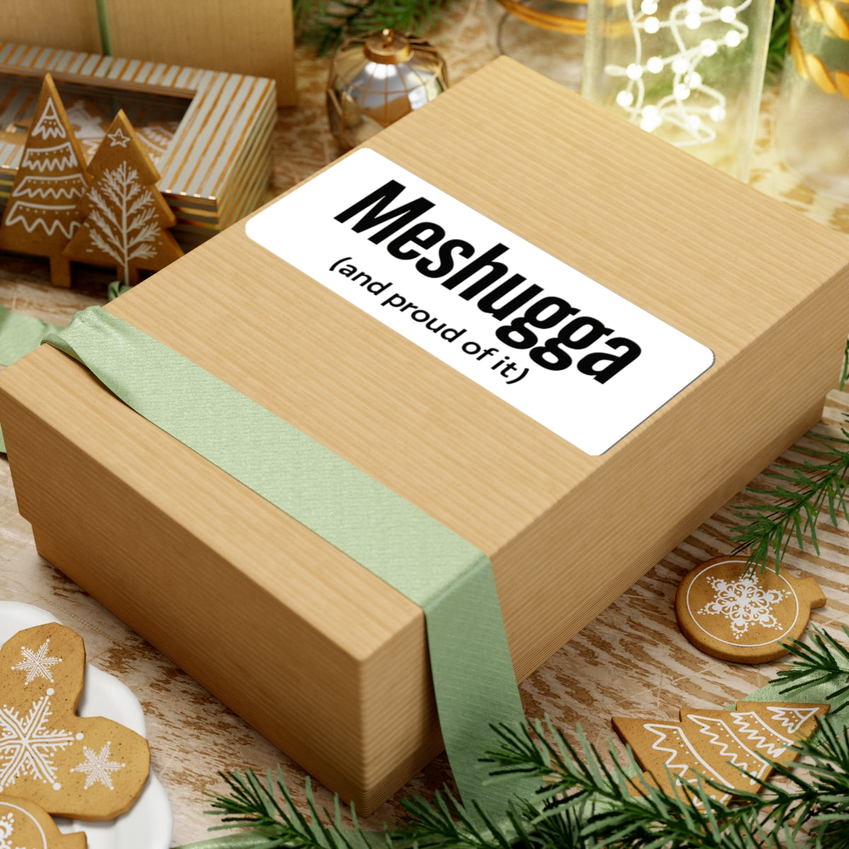 Wooden gift box with a green ribbon and 'Meshugga (and proud of it)' label, surrounded by Christmas decorations.