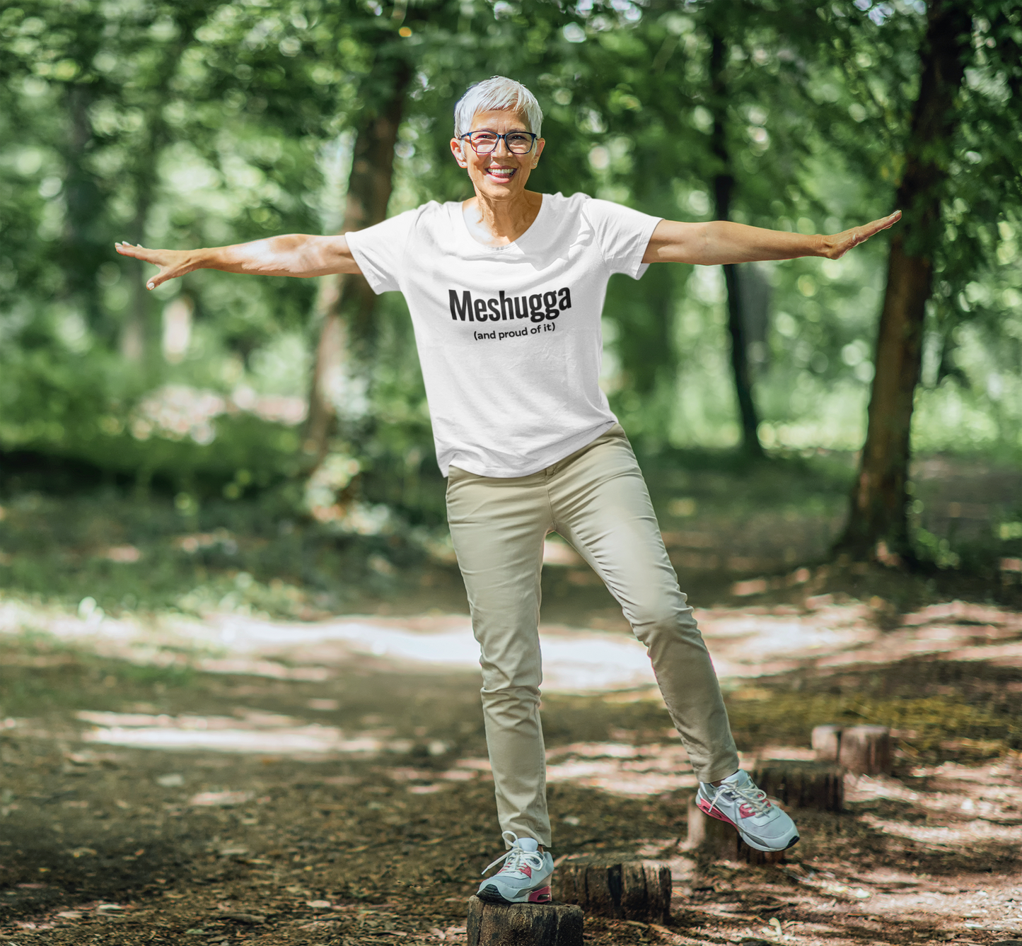Person wearing a 'Meshugga' t-shirt standing on a log in a forest