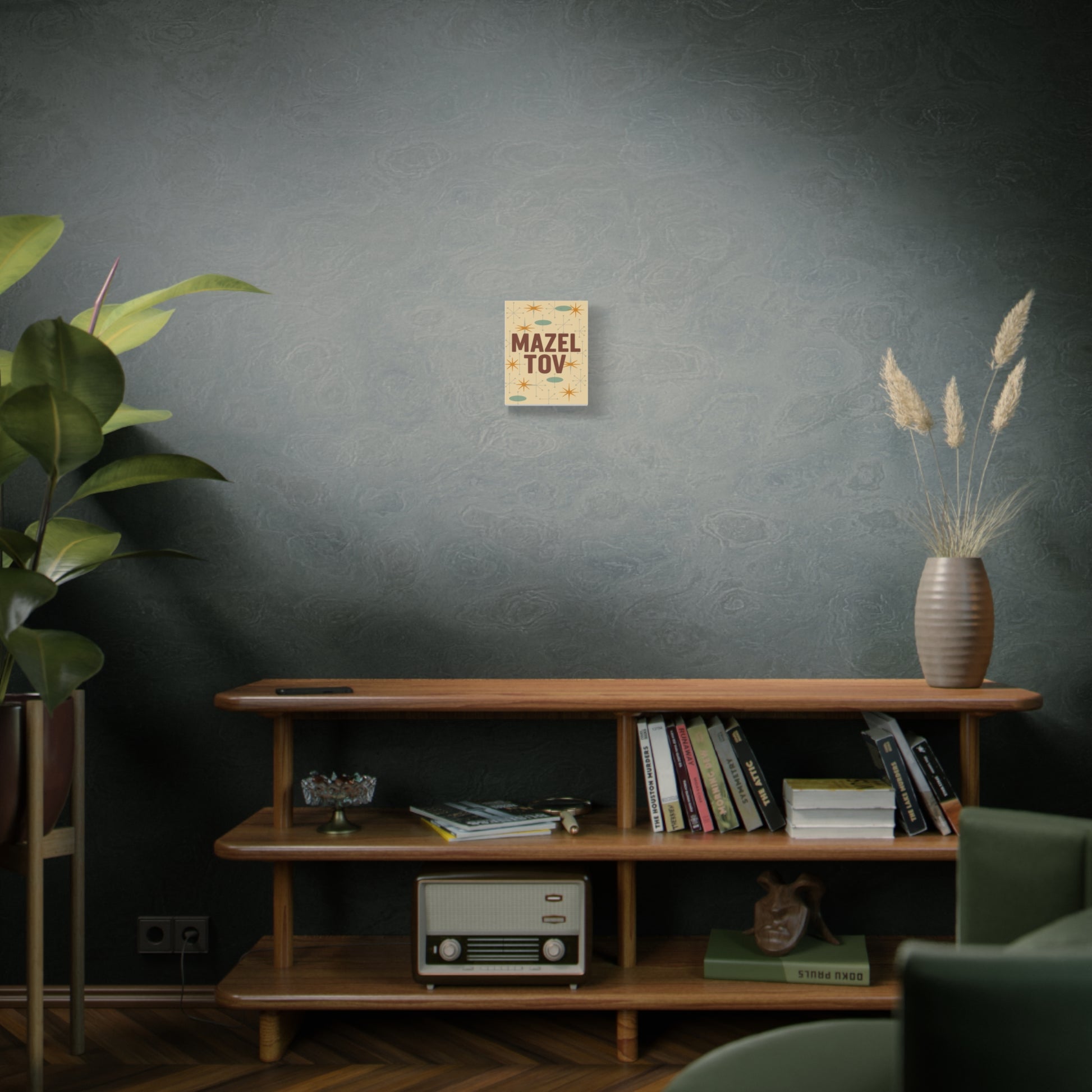 Living room with wooden shelf, books, plant, and a 'Mazel Tov" print against a dark wall.