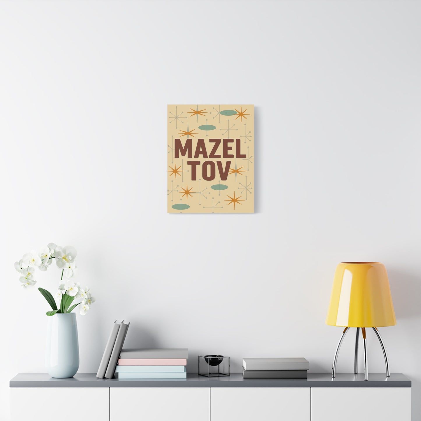 canvas print with 'Mazel Tov' text on a wall above a table with decor items.