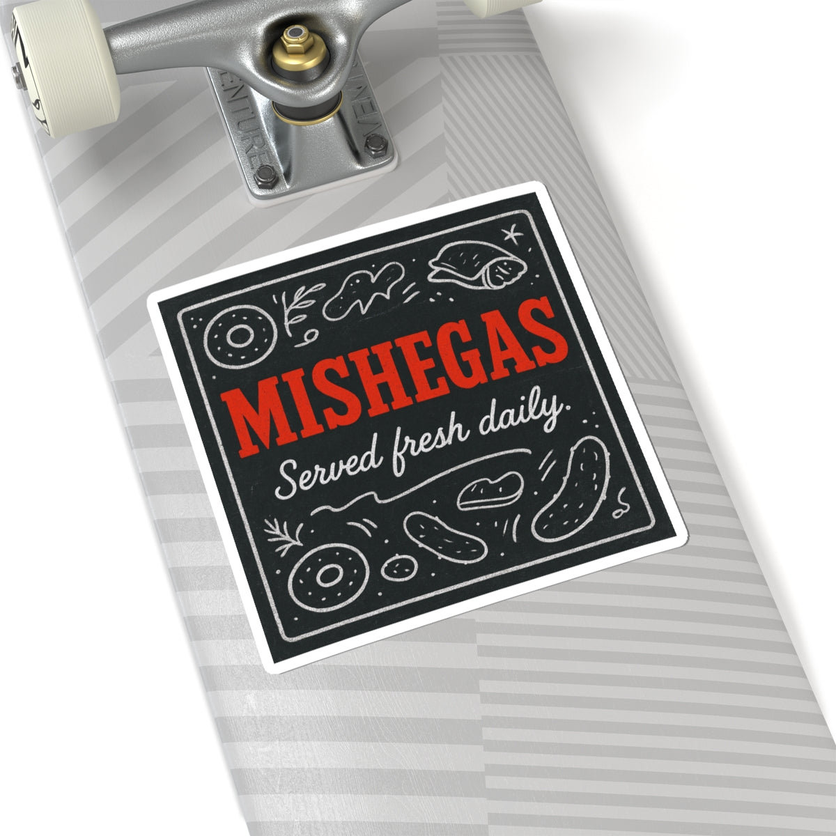 Skateboard with a sticker that reads 'MISHEGAS Served fresh daily' on a white background