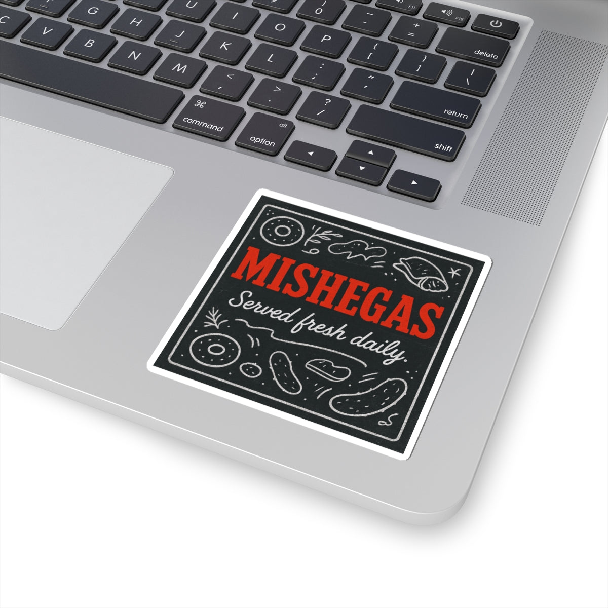 Sticker with 'Mishegas Served fresh daily' text on a laptop