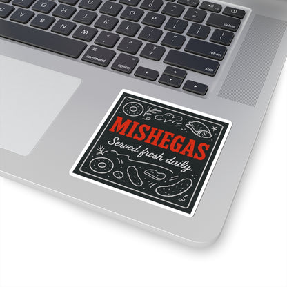 Sticker with 'Mishegas Served fresh daily' text on a laptop