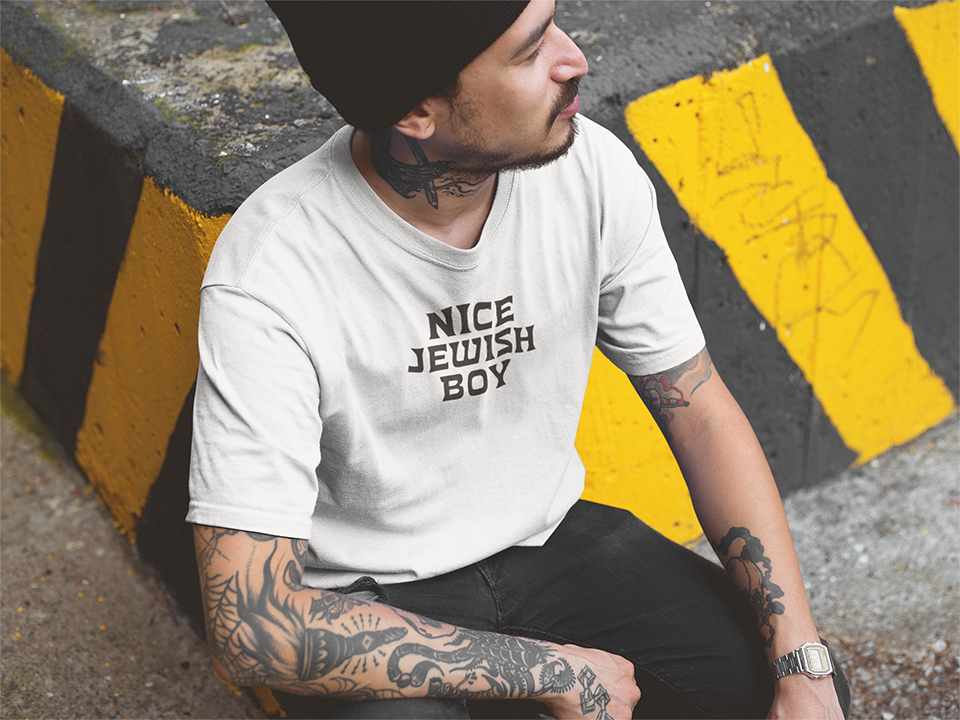 Person wearing a white t-shirt with 'Nice Jewish Boy' text, sitting on a yellow and black striped curb.