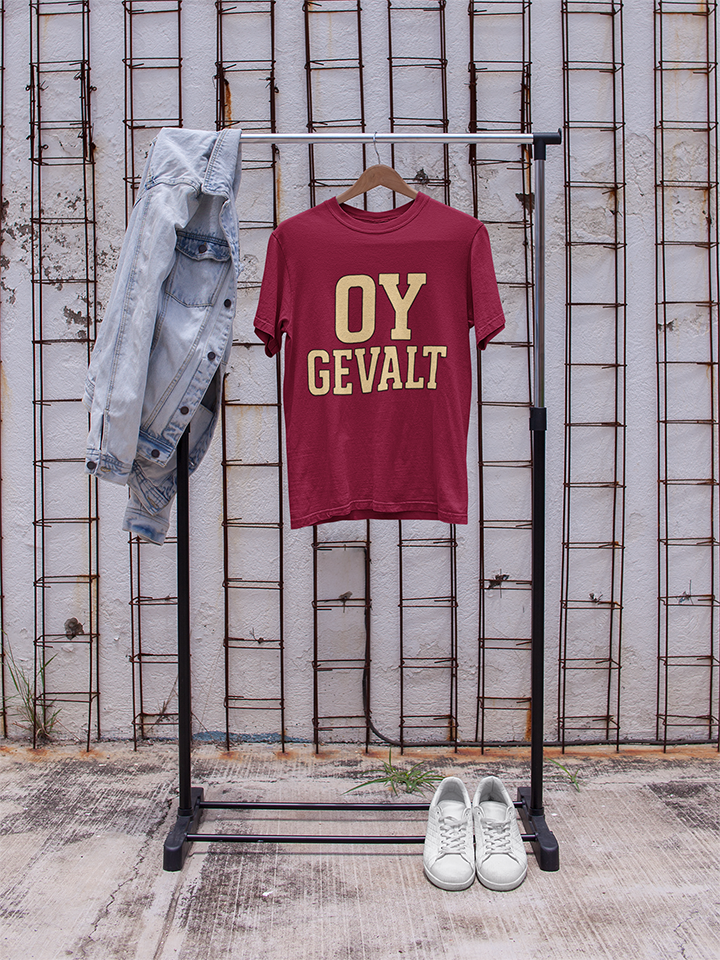Maroon t-shirt with 'OY GEVALT' text on a rack against a textured wall.