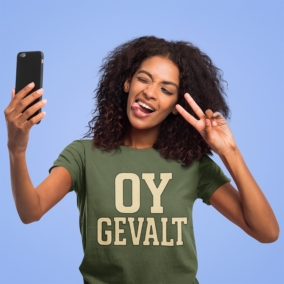 Woman wearing a green t-shirt with 'OY GEVALT' text, taking a selfie against a blue background