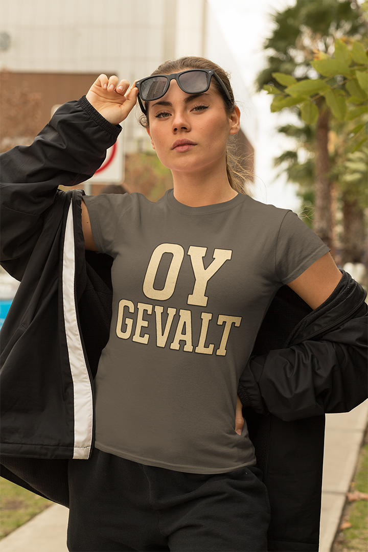 Person wearing a gray t-shirt with 'OY GEVALT' text, holding sunglasses, outdoors.