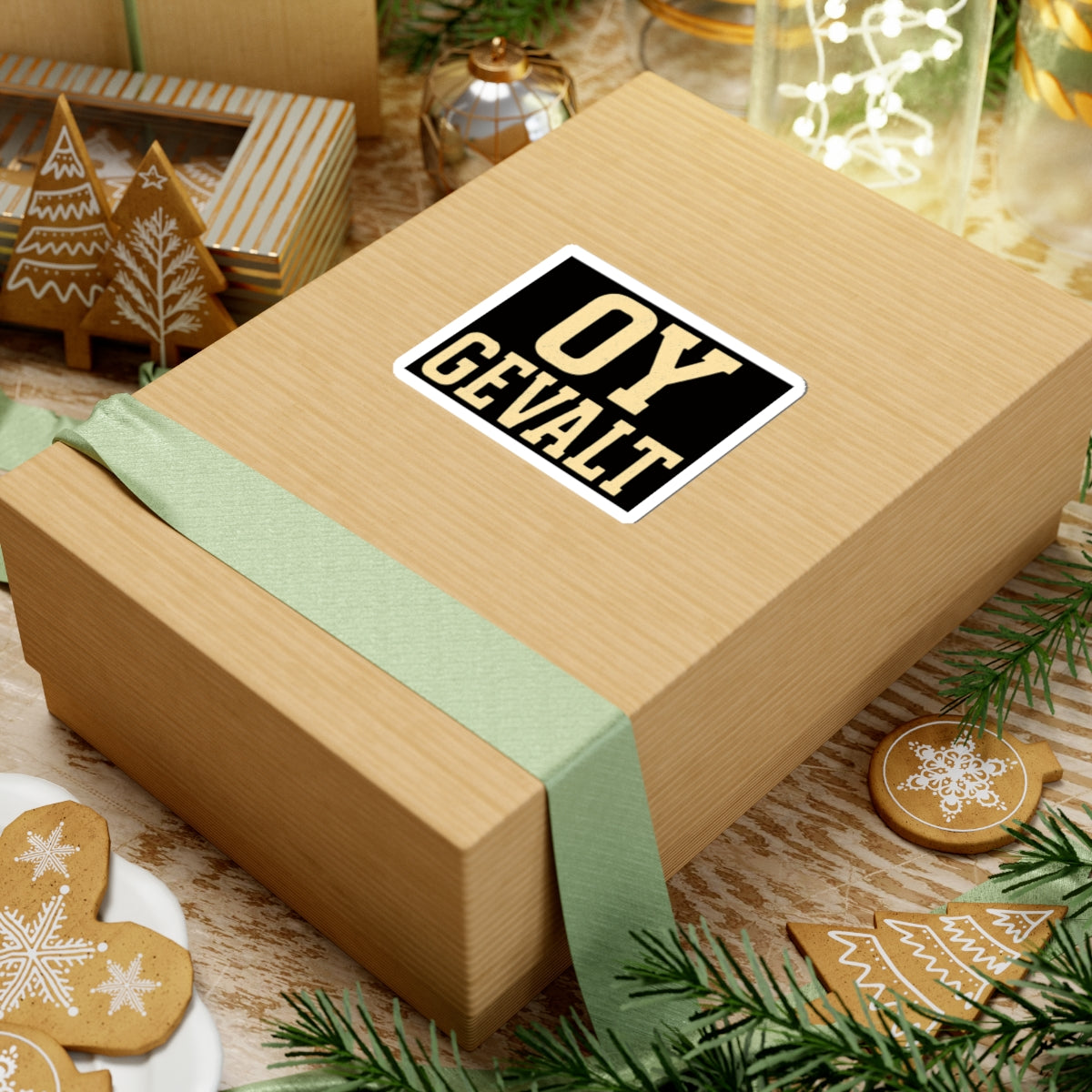 Wooden gift box with a green ribbon and 'OY GEVALT' sticker on a festive background with cookies and lights.