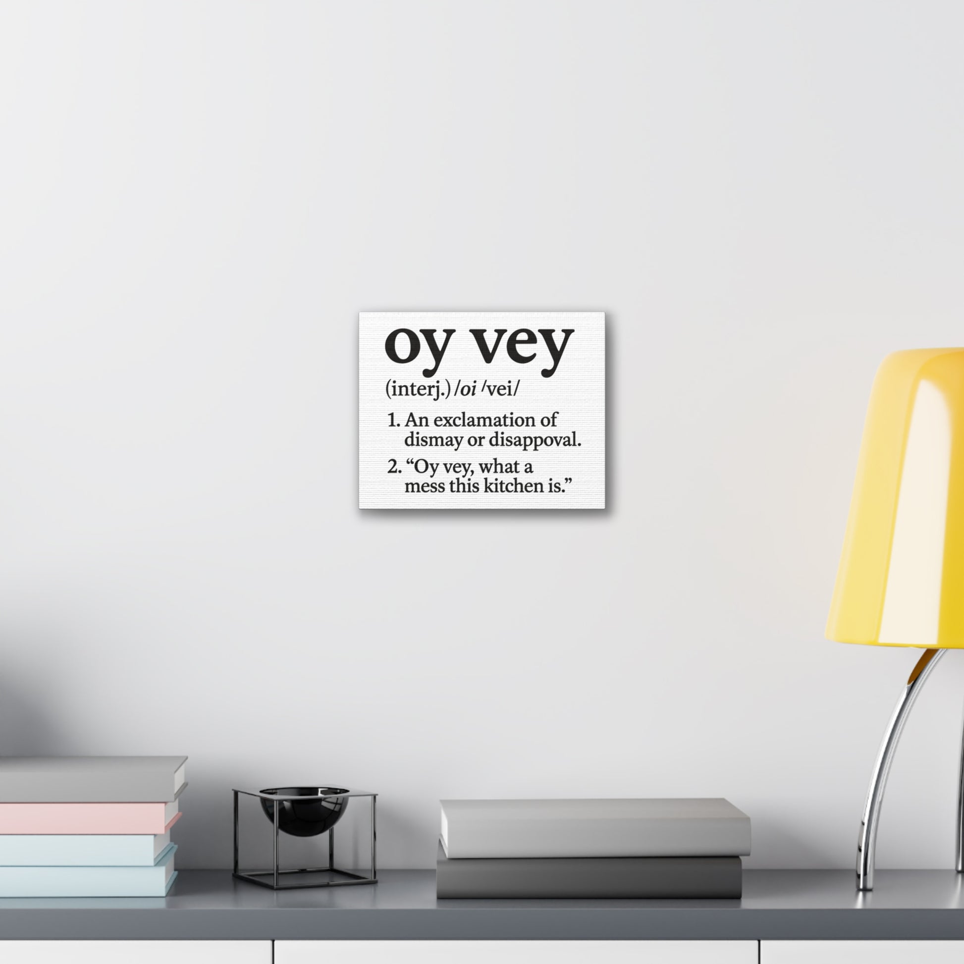 Decorative wall art with the word 'oy vey' definition on a white wall above a shelf.