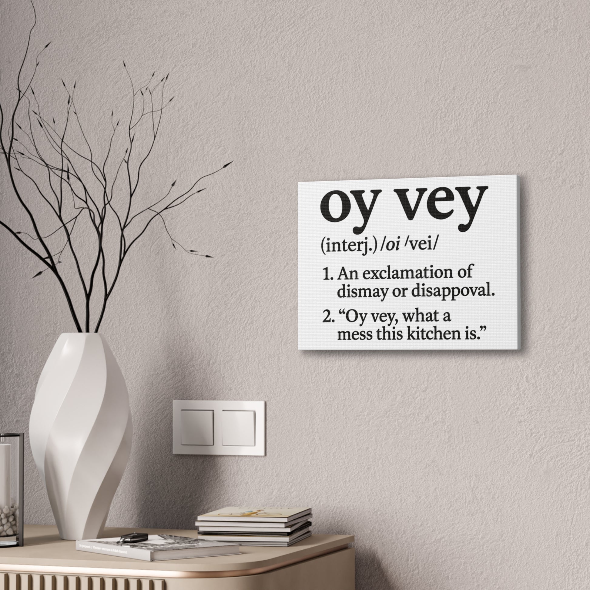 Canvas with 'oy vey' definition on a wall next to a vase and books.