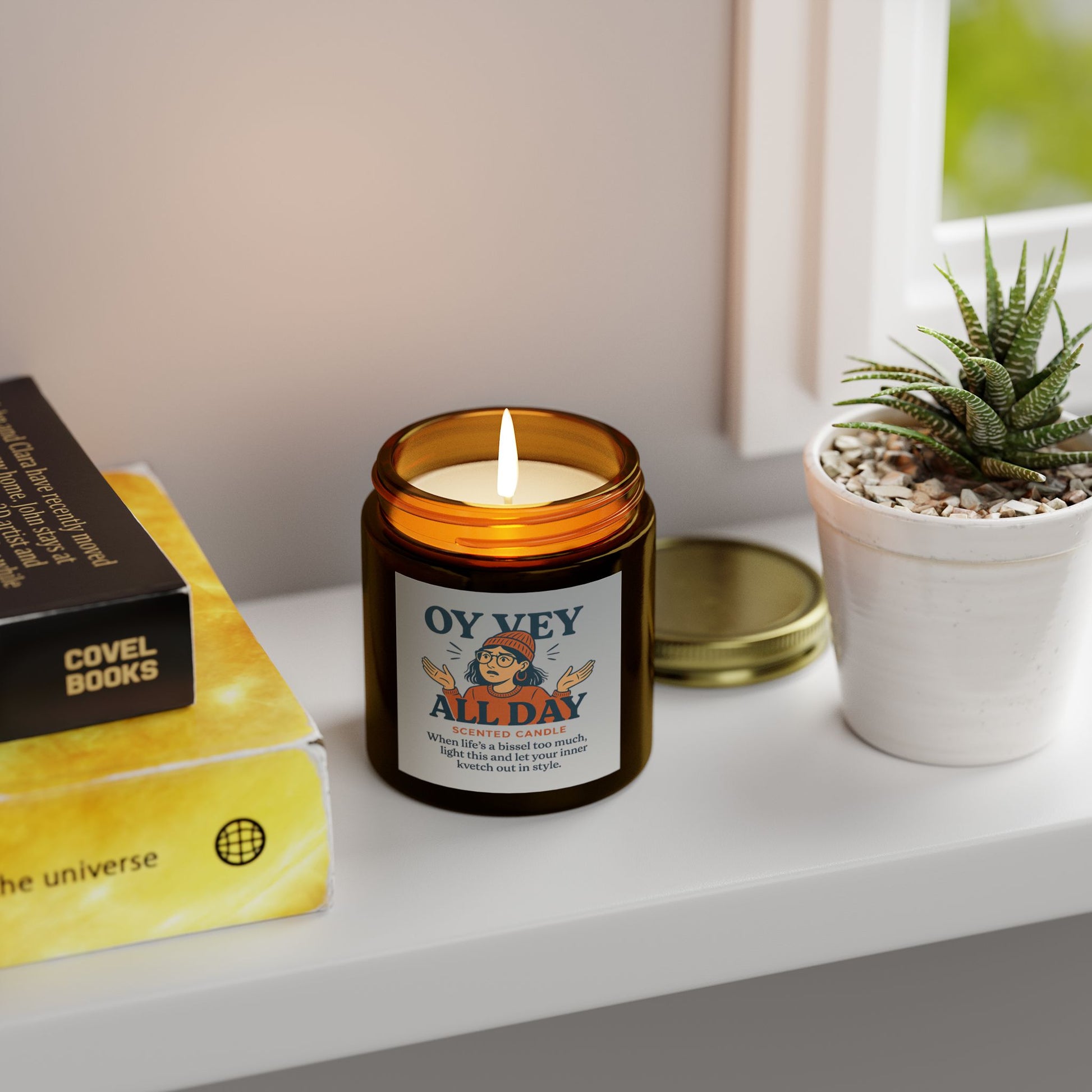 Candle labeled 'Oy Vey All Day' on a shelf with books and a plant