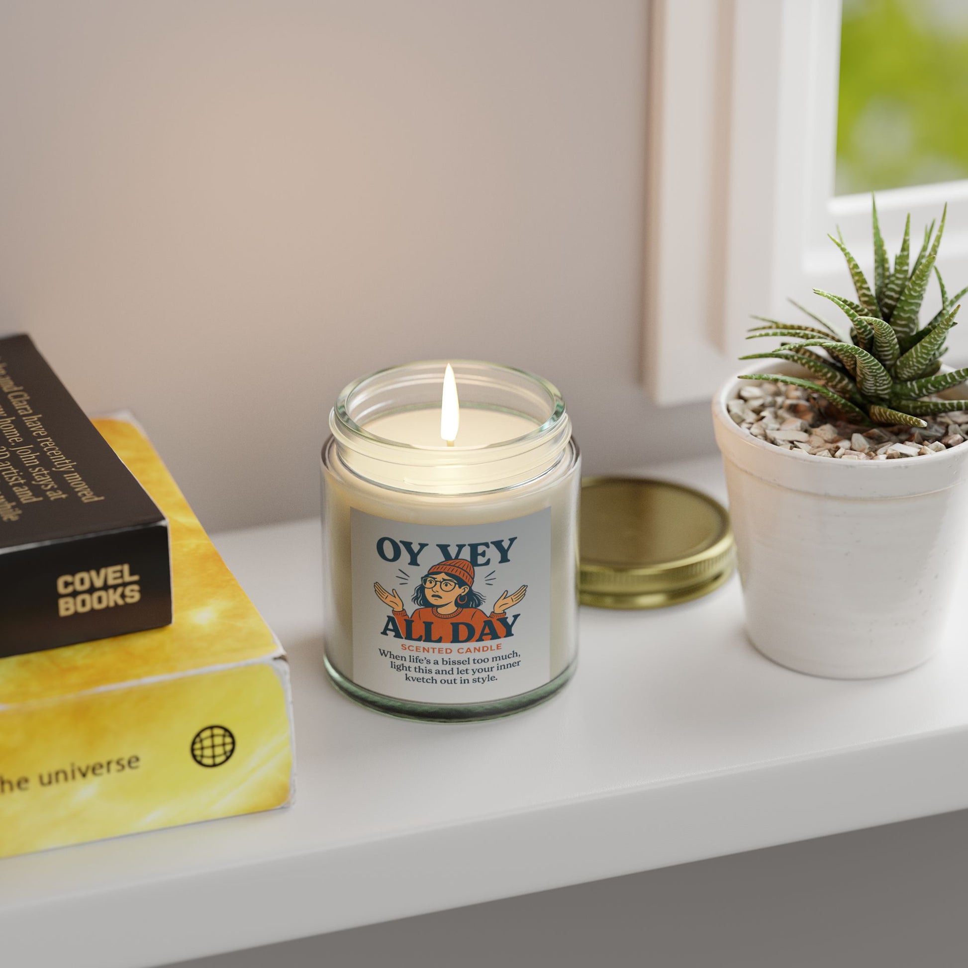 Candle labeled 'OY Vey All Day' on a shelf with books and a plant
