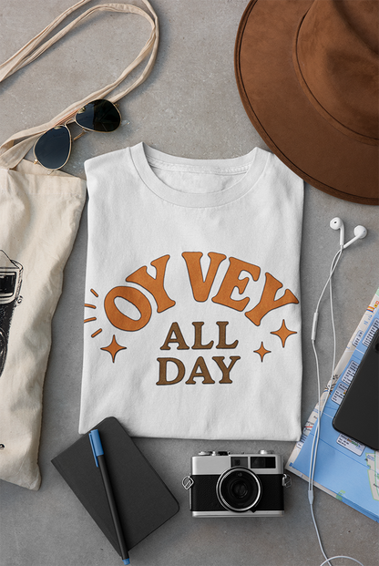 White t-shirt with 'Oy Vey All Day' text on a gray surface with accessories.
