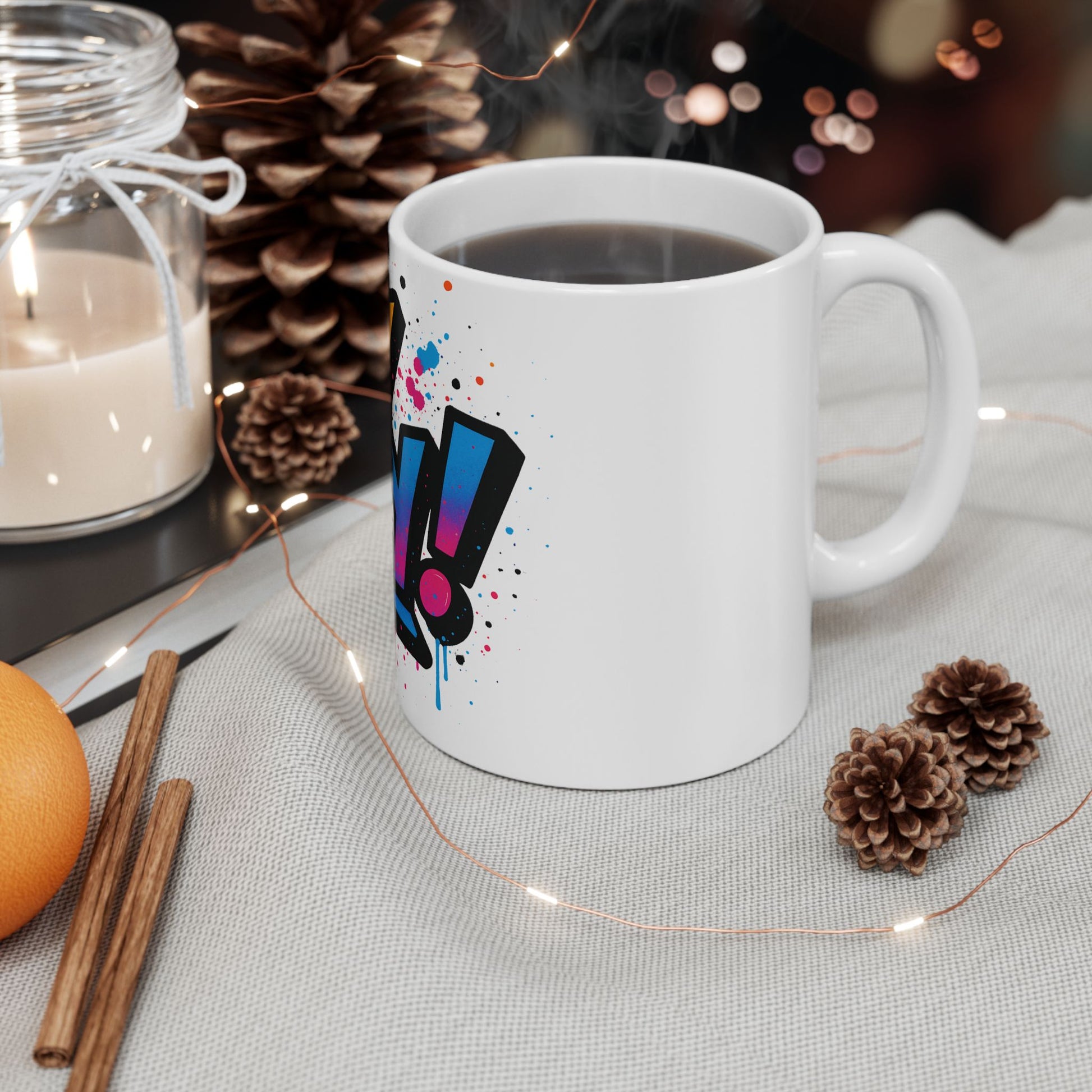 White mug with colorful 'oy vey' design on a table with candles, oranges, and pine cones.
