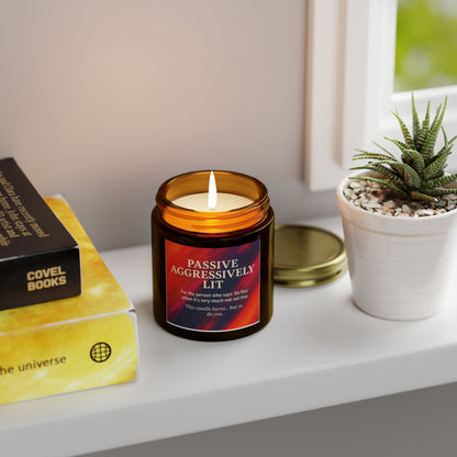 Candle with a humorous label on a shelf next to books and a plant