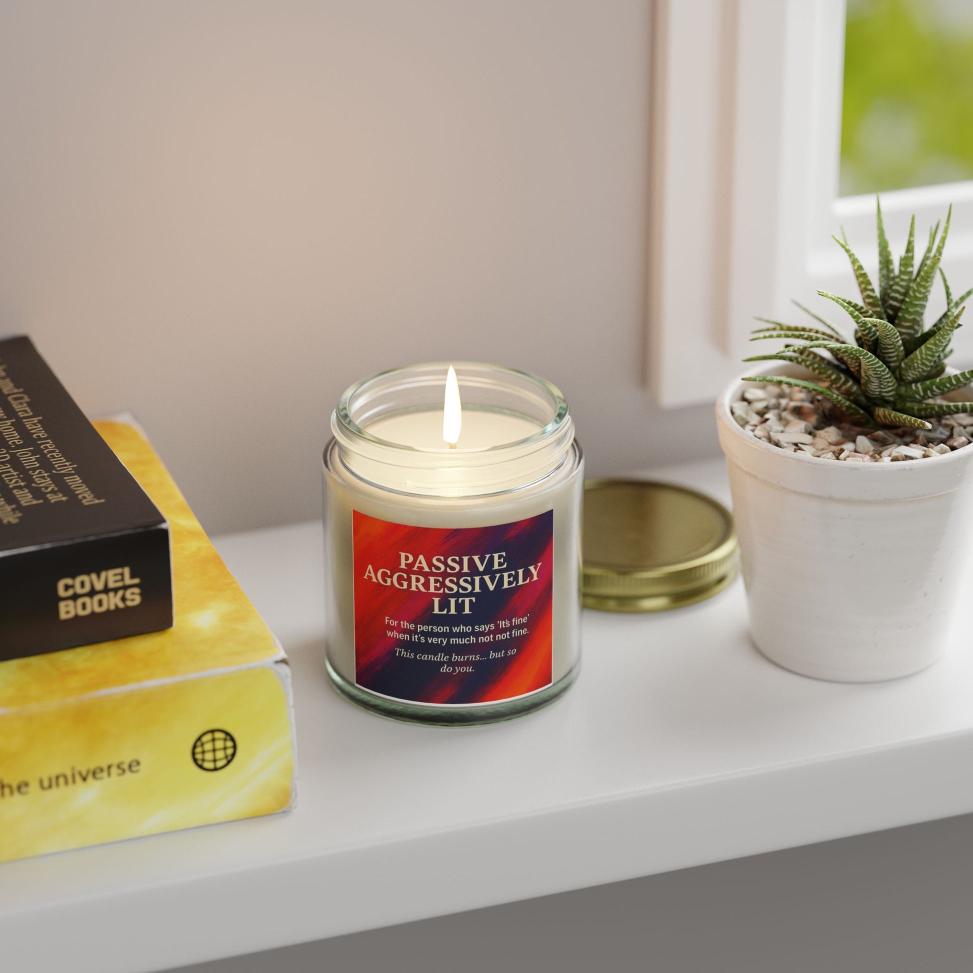 Candle with a red label on a shelf next to a book and plant