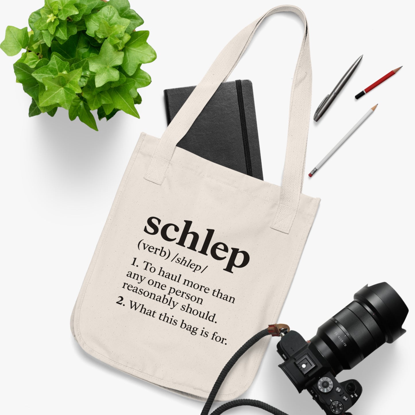 Beige tote bag with text, camera, notebook, and pens on a white background