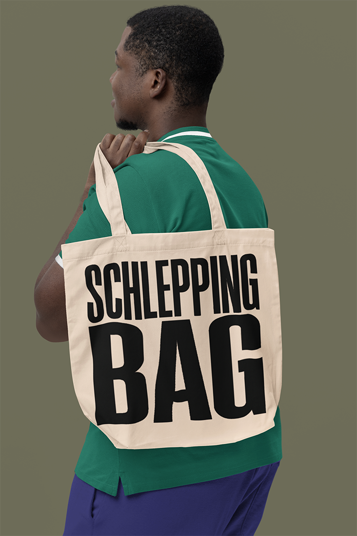 Man carrying a tote bag with 'SCHLEPPING BAG' text on a plain background