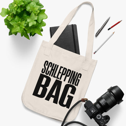 Beige tote bag with 'SCHLEPPING BAG' text, surrounded by stationery items on a white background