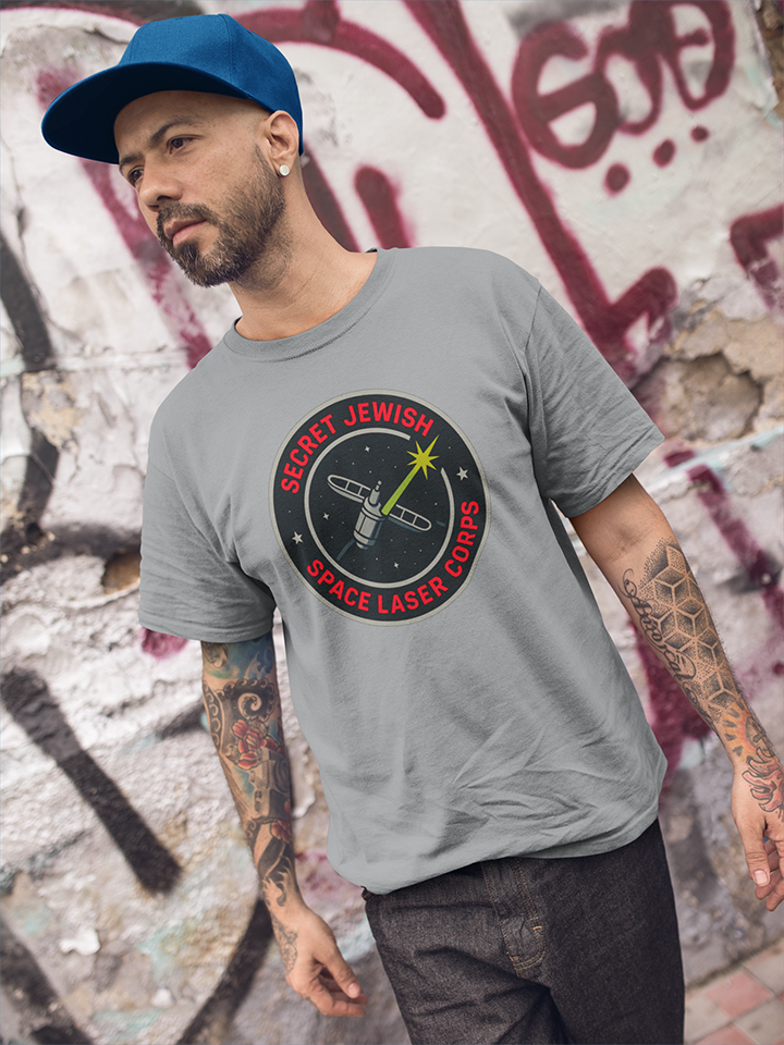 Man wearing a gray t-shirt with a graphic design in front of a graffiti-covered wall.