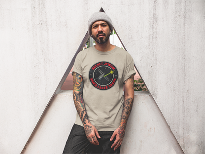 Man wearing a t-shirt with a logo and text, standing against a textured white wall.