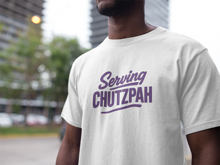Person wearing a white t-shirt with 'Serving Chutzpah' text in purple outdoors.