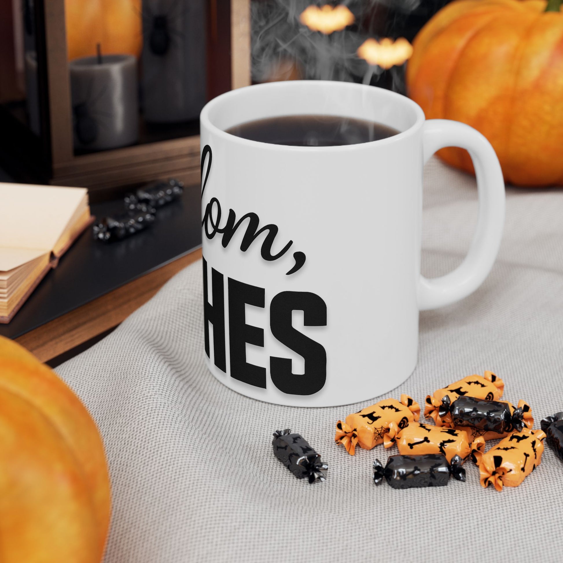 White mug with 'shalom, bitches' text on a table with Halloween-themed treats and pumpkins.