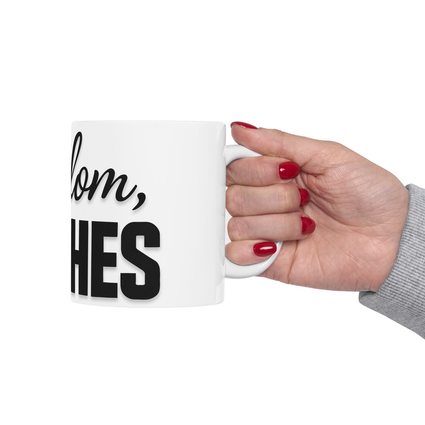 Hand holding a white mug with text 'shalom, bitches' on a white background