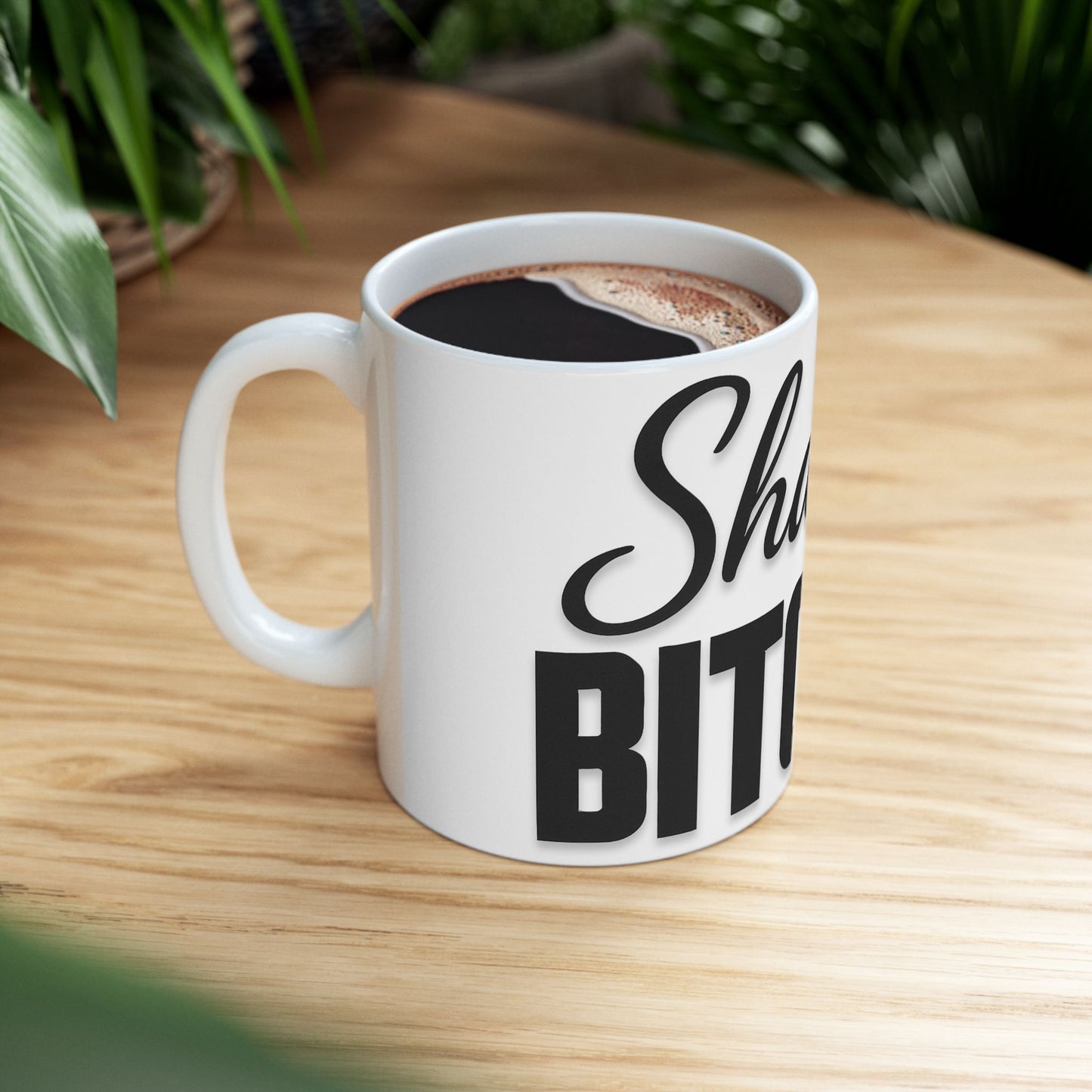White mug with black text 'shalom, bitches' on a wooden table