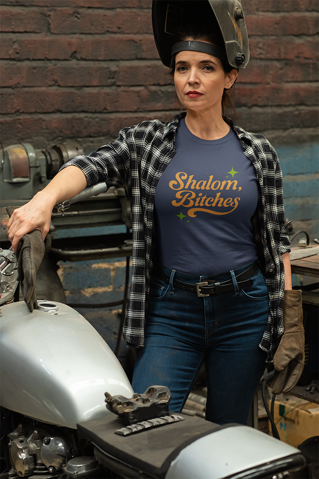 Person wearing a shirt with 'Shalom, Bitches' text in a workshop setting