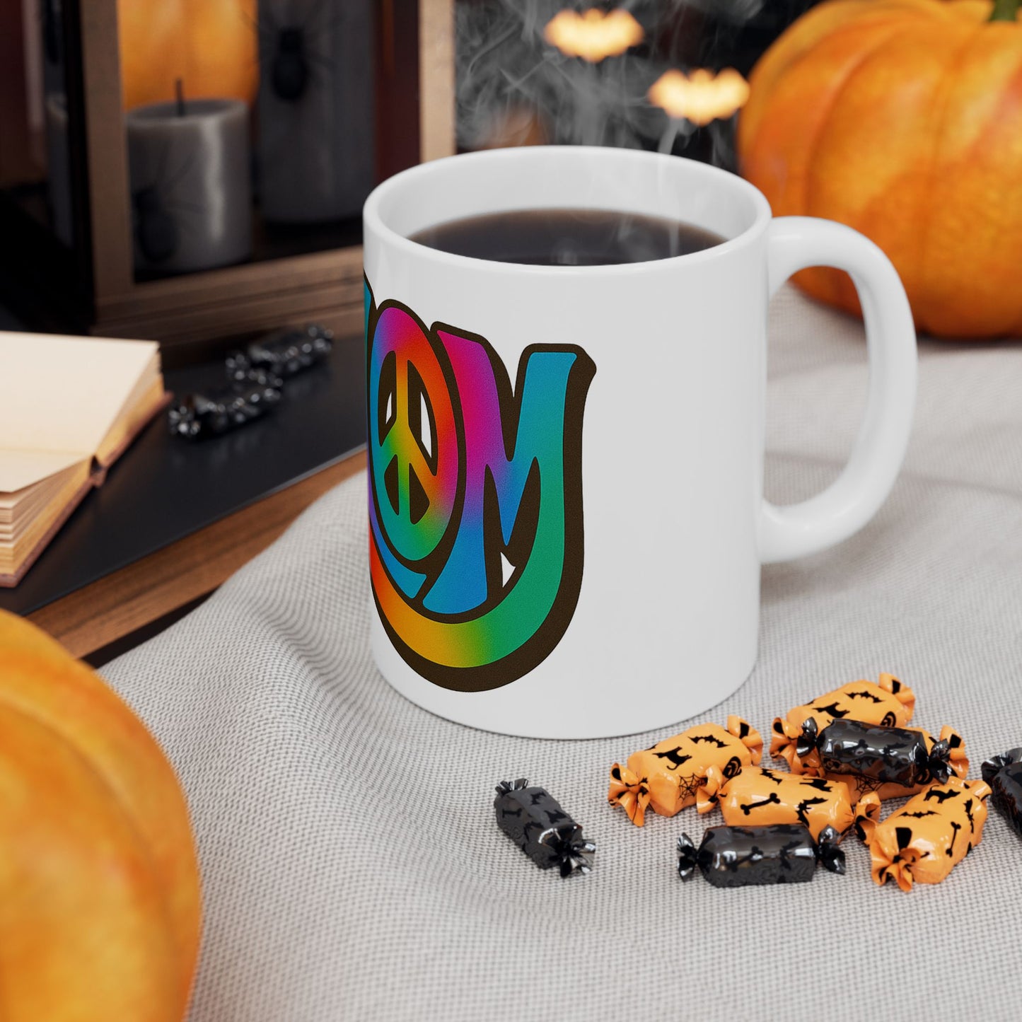 White mug with colorful 'shalom' design on a table with Halloween-themed treats and pumpkins.