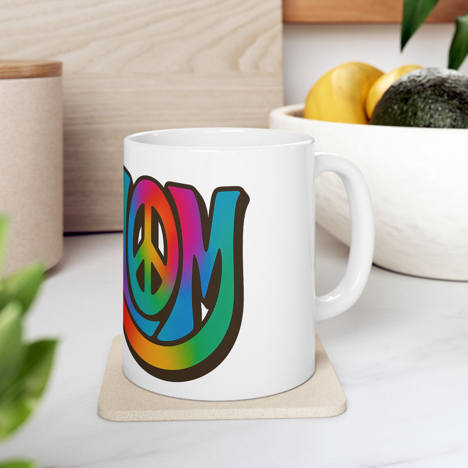 White mug with colorful 'shalom' design on a white surface with plants and a bowl in the background