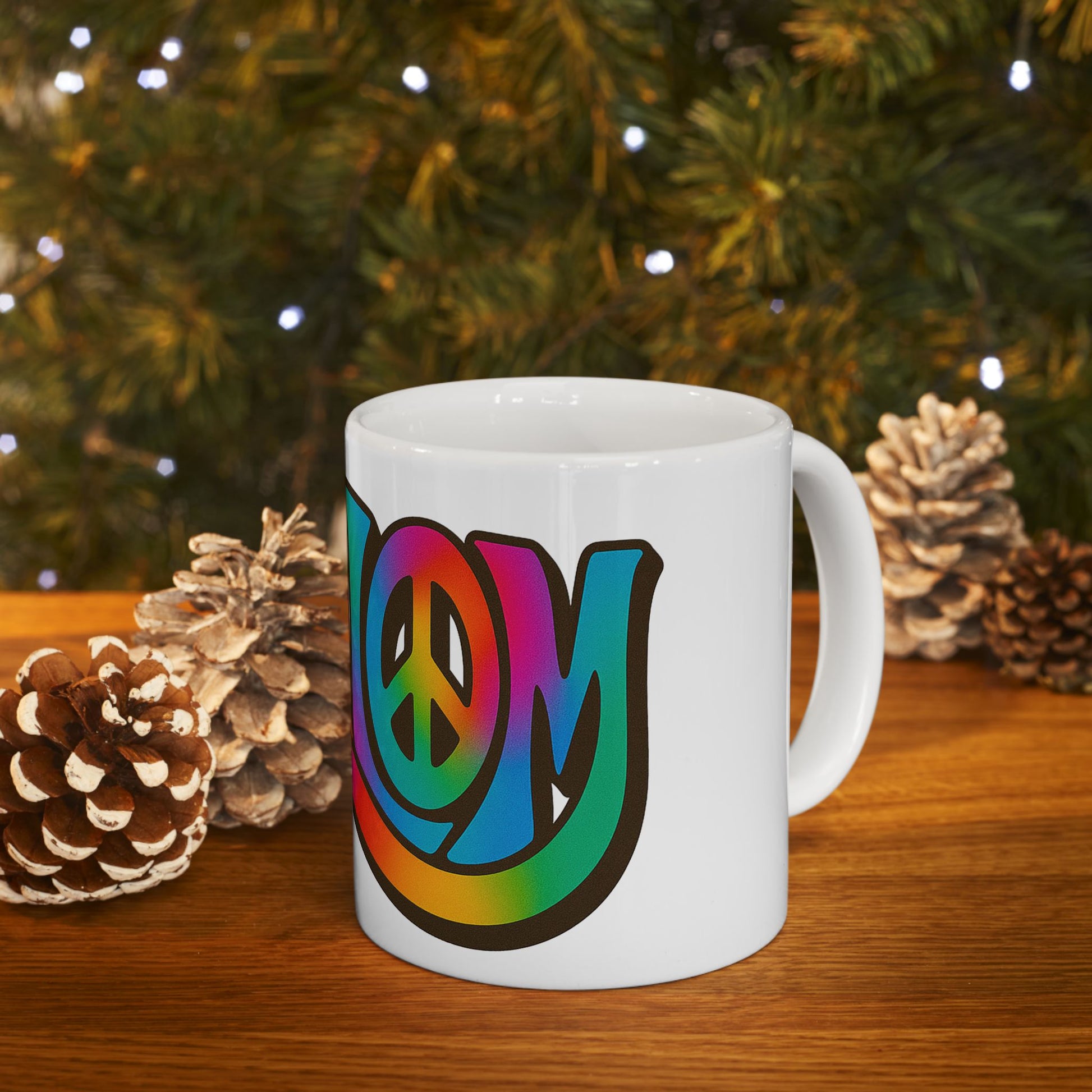 White mug with rainbow 'shalom' design on a wooden surface with Christmas decorations.