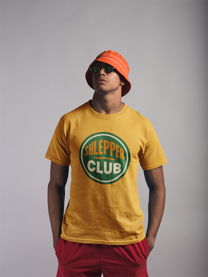 Person wearing a yellow 'Shlepper Club' t-shirt with an orange bucket hat and sunglasses on a gray background