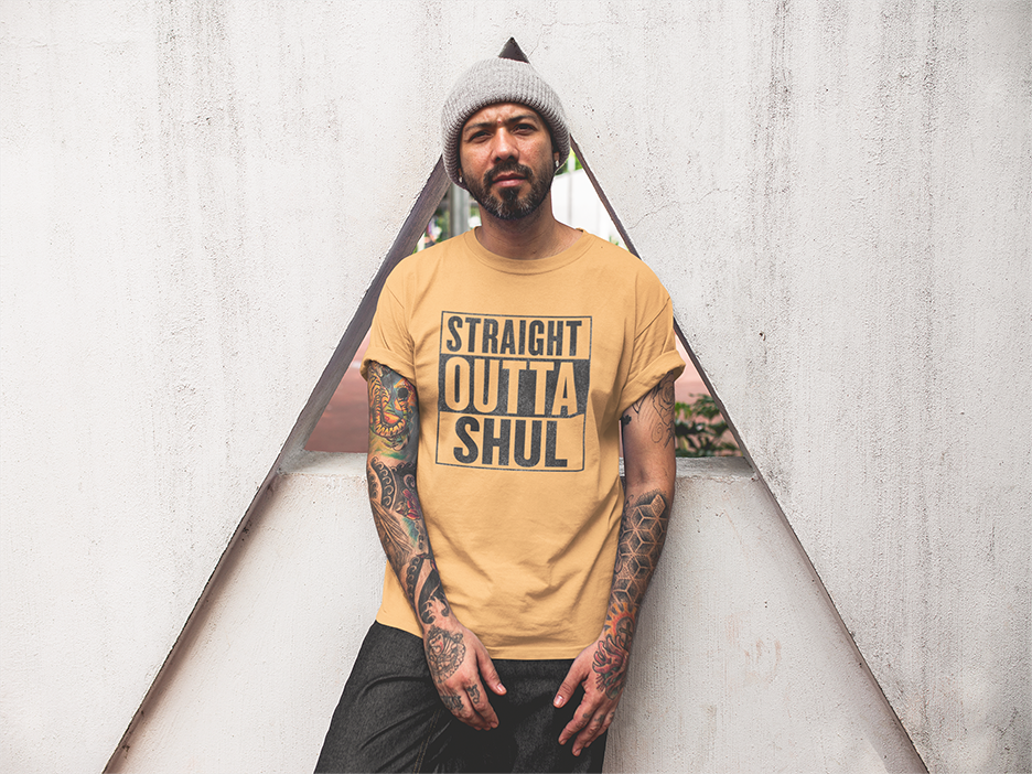 Man wearing a yellow t-shirt with 'Straight Outta Shul' text, standing against a textured wall.