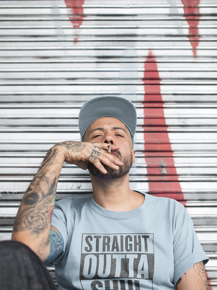 Man wearing a cap and t-shirt with text, sitting against a metal shutter background