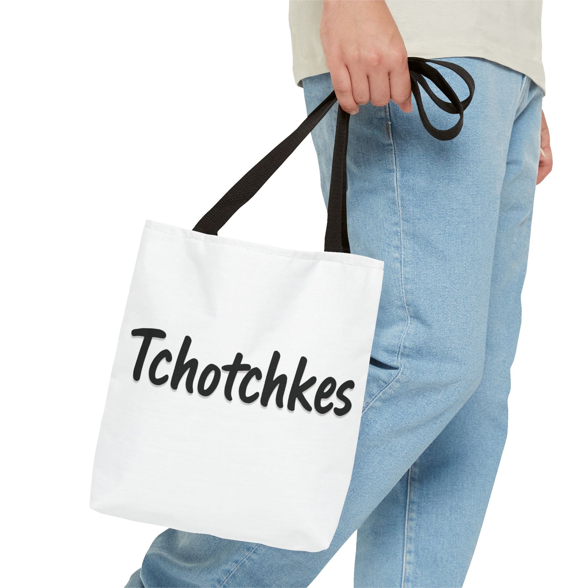 White tote bag with 'Tchotchkes' text held by a person wearing light blue jeans.