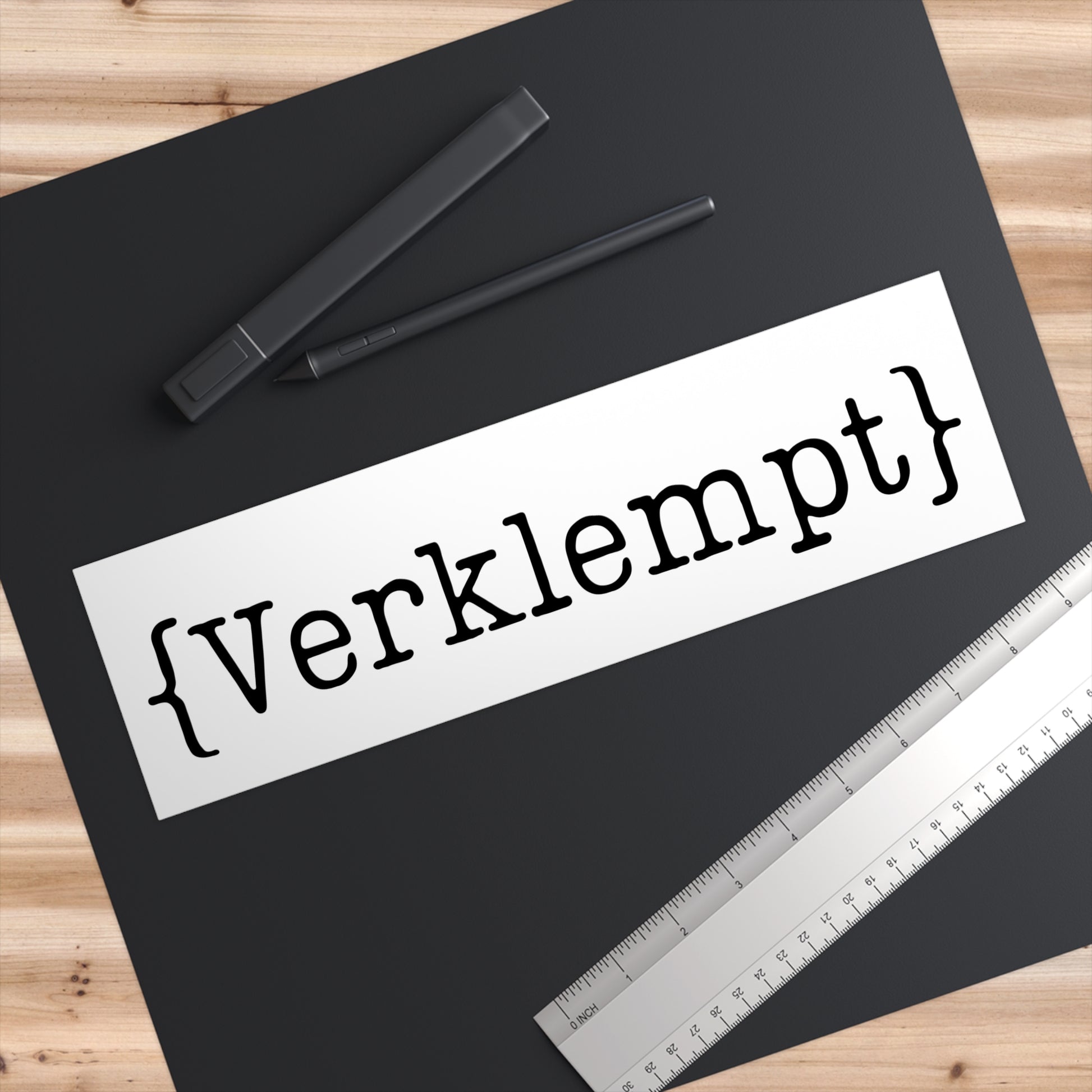 Sheet of paper with 'Verklempt' text on a black surface with pens and a ruler.