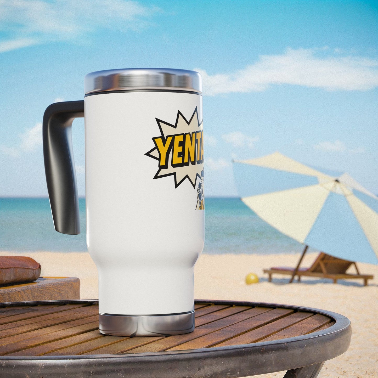 White travel mug with a 'yenta' design on a beach table with ocean and umbrella in the background