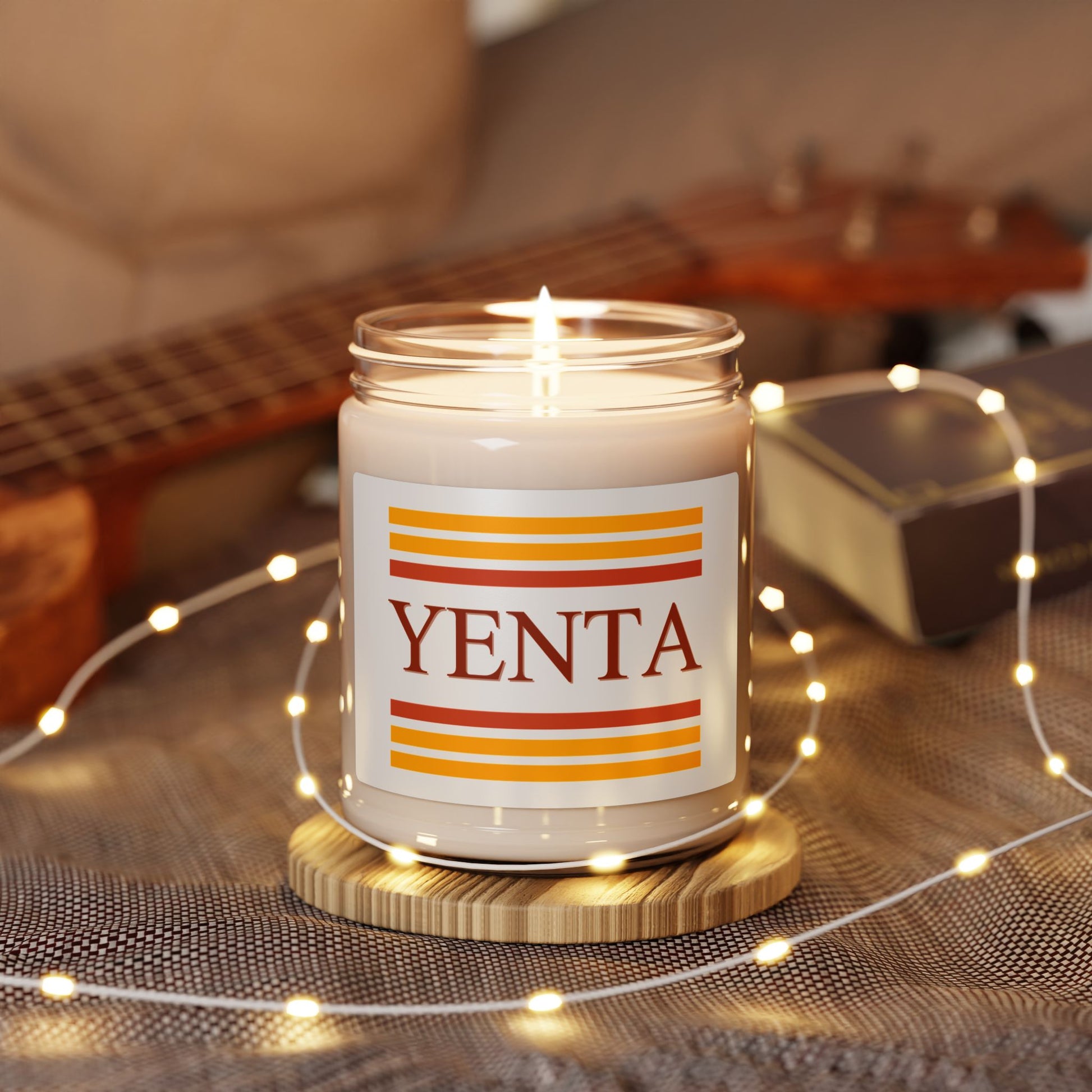 Candle with 'Yenta' label on a wooden coaster surrounded by string lights and a guitar in the background