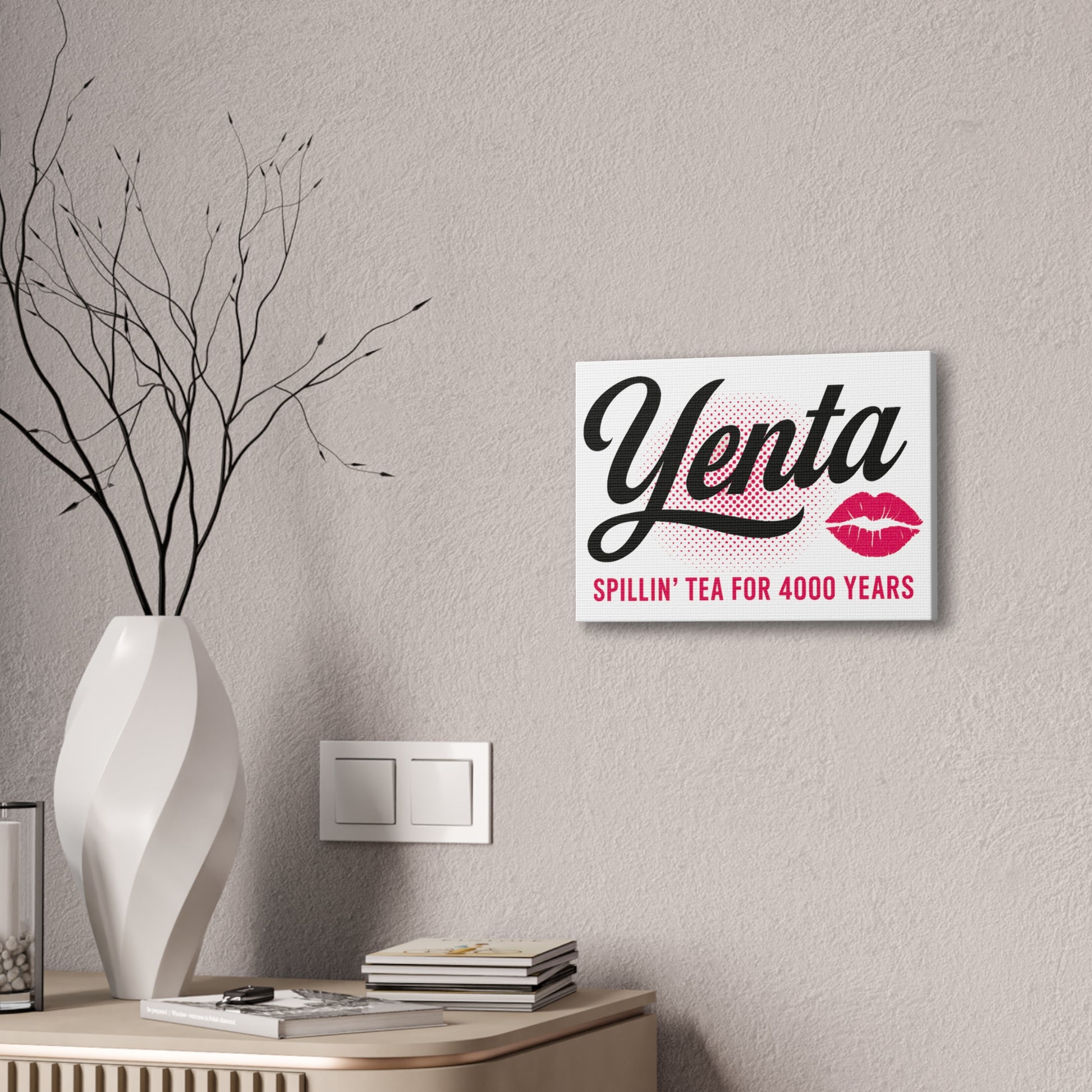 Decorative wall sign with 'Yenta' text on a neutral wall with a vase and books below.