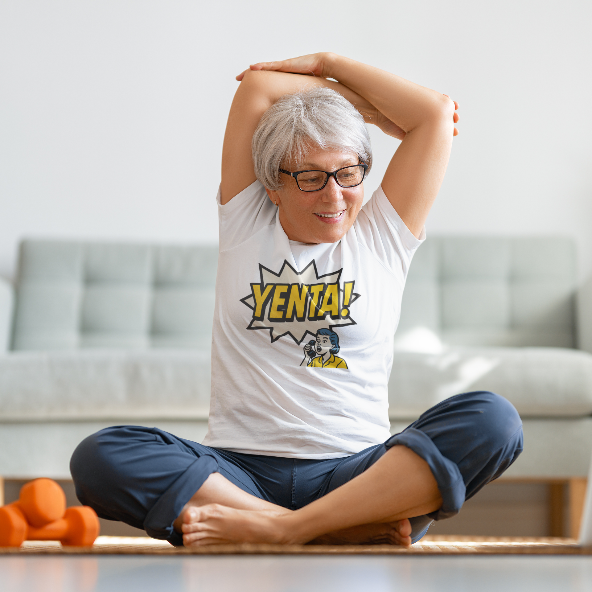Person stretching in a living room wearing a white t-shirt with 'YENTA!' design.